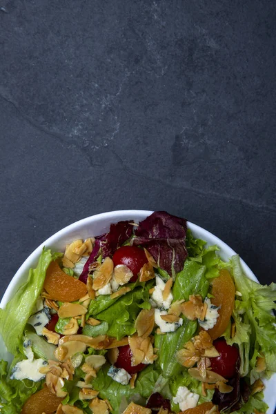 Bir tabak yeşil yapraklı, domatesli, peynirli, bademli ve kayısılı salata. metin alanı