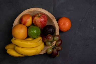 Tahta yalak, çeşitli meyveler, siyah taş arka planda. Metin için boşluk
