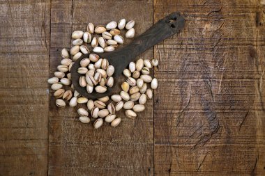 Ahşap masada tahta kaşıkta fıstıklı bir porsiyon. Metin için boşluk
