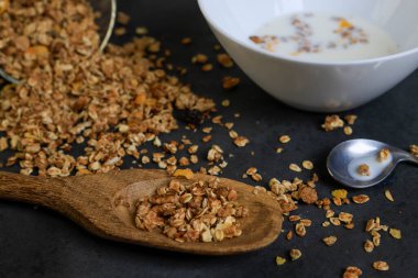 Tahıl taneleri siyah zemine saçılmış, süt tabağı ve tahta kaşıkla.