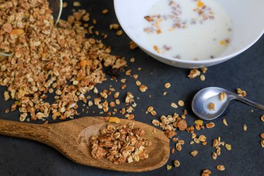 Tahıl taneleri siyah zemine saçılmış, süt tabağı ve tahta kaşıkla.