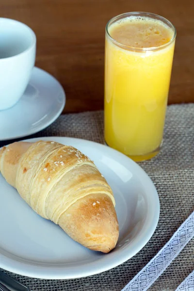 クロワッサンの種類のパン 素朴なジュートテーブルクロス上の料理で 背景にオレンジジュースのカップと — ストック写真