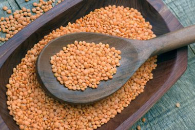 Ahşap kaşıkta pembe mercimek ve ahşap masa üzerinde ahşap tepsi.