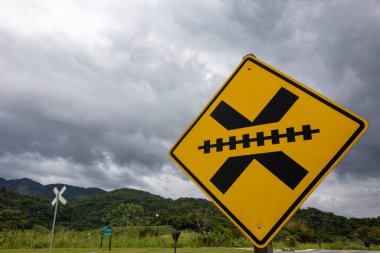 Trafik levhası: Demiryolu hattını geçmek, arka planda yağmur bulutları. Brezilya 'nın kırsalında