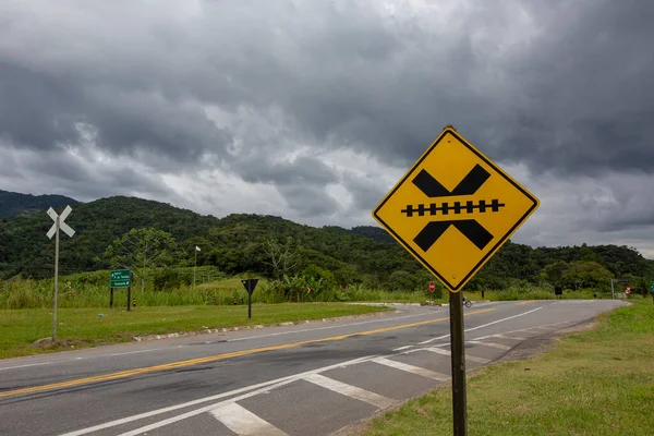 Trafik levhası: Demiryolu hattını geçmek, arka planda yağmur bulutları. Brezilya 'nın kırsalında