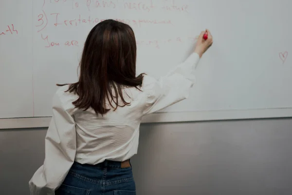 Vue arrière d'un jeune professeur d'anglais mignon en chemisier blanc écrivant sur une planche et donnant une classe — Photo