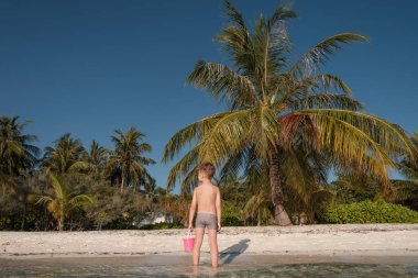 Bir çocuk kumsalda pembe bir kovayla oynuyor..