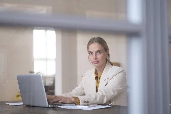 Фото женщины-предпринимательницы, одетой в формальную одежду, смотрящей в камеру во время работы и сидящей за столом в офисе, изолированном на белом фоне — стоковое фото
