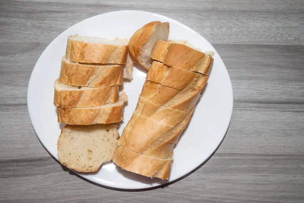 Trozos de pan en rodajas en un plato blanco brillante. Fondo de madera gris oscuro —  Fotos de Stock