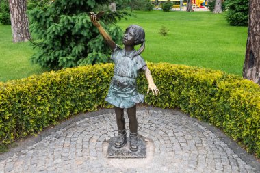 Kharkiv, Ukrayna - 6 Haziran 2021. Kolunu uzatmış küçük bir kuşu tutan küçük bir kız. Parkta yeşil çalılar ve çimenler olan bronz bir heykel.