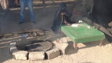 Hurghada, Mısır - Ocak 2022: Peçeli bir kadın ateşin üzerinde ekmek hazırlıyor. Bedevi hayatı.