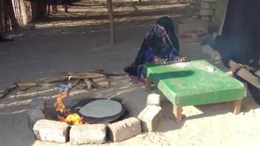 Hurghada, Mısır - Ocak 2022: Peçeli bir kadın ateşin üzerinde ekmek hazırlıyor. Bedevi hayatı.
