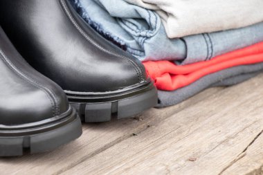 Kalın tabanlı kadın yüksek siyah çizmeleri ve bir yığın şey sokakta, güneşin altında bir tahtanın üzerinde duruyor kadın ayakkabıları ve kışlık giysiler, şık kıyafetler ve ayakkabılar, eşyalar.