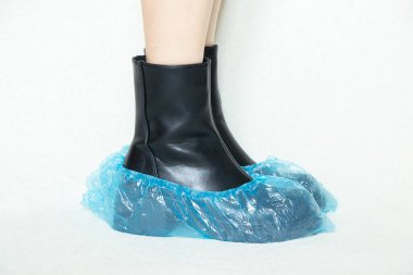 Siyah çizmeli, beyaz arka planda, tek kullanımlık botları, kadın ayakkabıları, yerde ayakları, Bohilas 'taki bir hastanede beyaz arka planda botları olan kadın.