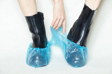 Siyah çizmeli, beyaz arka planda, tek kullanımlık botları, kadın ayakkabıları, yerde ayakları, Bohilas 'taki bir hastanede beyaz arka planda botları olan kadın.