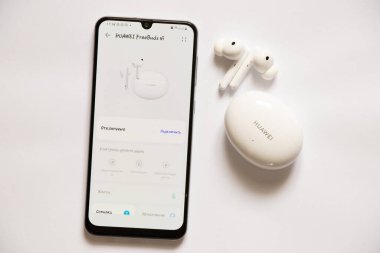 Ukrayna Dnipro 08.10.2021 - Yeni Huawei FreeBuds 4i Beyaz kulaklıklar paketin içinde telefonun yanında beyaz bir arka planda uzanıyor ve kulaklık, kablosuz kulaklık ve uygulamalar için mobil uygulamalar açık