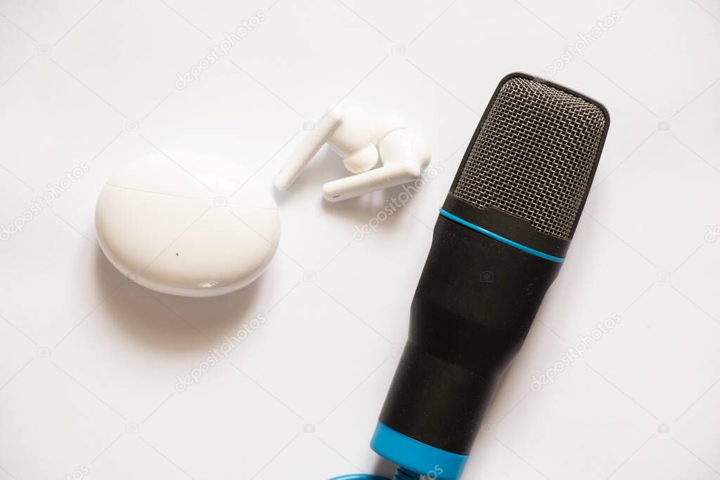 case with wireless earphones in the shape of an oval and earphones lies lying around a microphone on an isolated background, wireless earphones, music