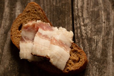 Bir parça siyah ekmek ve dilimlenmiş pastırma tahtadan bir masanın üzerinde, pastırmalı ekmek