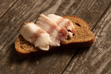 Bir parça siyah ekmek ve dilimlenmiş pastırma tahtadan bir masanın üzerinde, pastırmalı ekmek