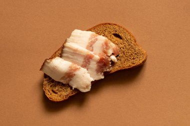 Bir dilim siyah ekmek ve dilimlenmiş pastırma kahverengi arka planda, pastırmalı ekmek.