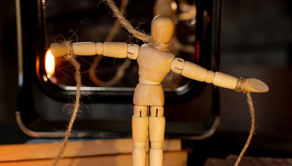 a wooden man on ropes tied to a man's hand, manipulation of people and slavery, free will, power over people