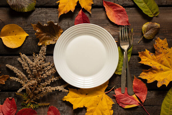dinner plate stands on the table in autumn yellow-red leaves, autumn decor from the table, cutlery, table decorations
