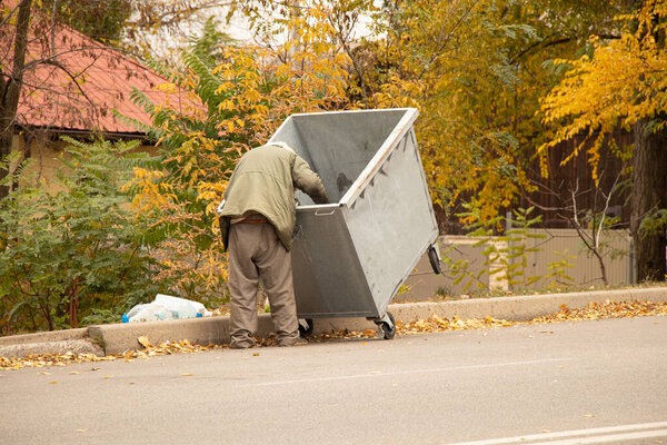 грязный бездомный, ищущий еду в мусорном баке, бездомный и мусорные отходы, ищущий еду, блуждающий человек