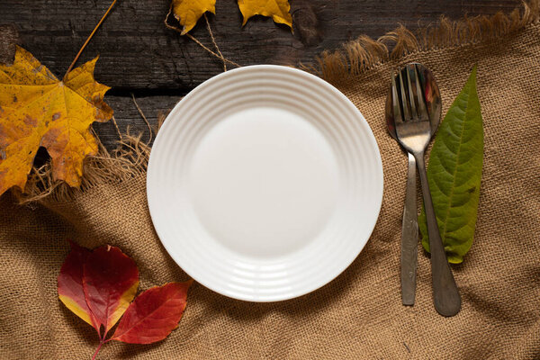 dinner plate stands on the table in autumn yellow-red leaves, autumn decor from the table, cutlery, table decorations