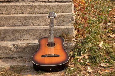 Eski kahverengi gitar parkta yatıyor sonbaharda merdivenlerde, gitarda.