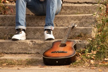 Eski kahverengi gitar parkta güneşin altında bir adamın merdivenlerinde yatıyor, gitar, hobi.