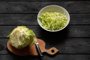 Genç yeşil lahana bir kasede kesilmiş ve tahta bir tahtanın üzerinde, siyah ahşap bir masada lahana salatası