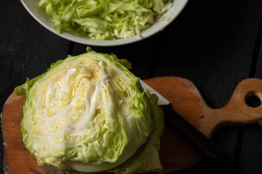 Genç yeşil lahana bir kasede kesilmiş ve tahta bir tahtanın üzerinde, siyah ahşap bir masada lahana salatası