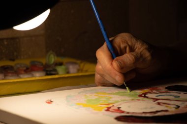 Yaşlı kadın, bir lambanın ışığında yağlı boya tuvale resim çizer, evde resim çizer, sanat ve hobiler, büyükannenin hobileri.