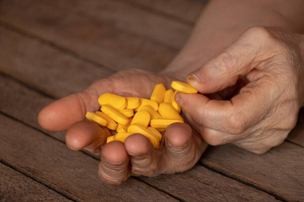 grandmother holds yellow pills in her hands on a wooden table, pills in hands and women lying and medicine