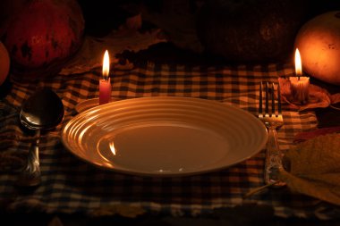 Balkabağı ve sonbahar yapraklarının arka planında, masada boş bir tabak duruyor, mum ışığında akşam yemeği, sonbahar masası dekoru, mum ışığında şenlik masası