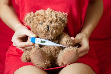 Elinde bir termometreyle elinde kahverengi bir oyuncak ayı tutan bir kız. Yatak odasında, yatakta, çocukluk hastalığında, ateşinde ve ateşinde dünya çapında bir salgın.