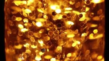 Altın parıltılar lambada yavaşça süzülür, parıltılı lav lambası, arka plan için yavaş çekimde altın şekerler, şenlikli yeni yıl