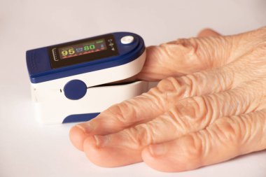 İzole edilmiş arka plandaki bir kadının parmağındaki nabız oksimetresi kandaki oksijen seviyesini ölçer.