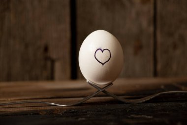 Kalp, eski ahşap bir masanın çatallarında duran tavuk yumurtasının üzerine çizilir. Aşk ve duygular.