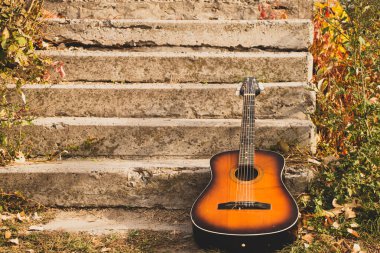 Eski kahverengi gitar parkta yatıyor sonbaharda merdivenlerde, gitarda.