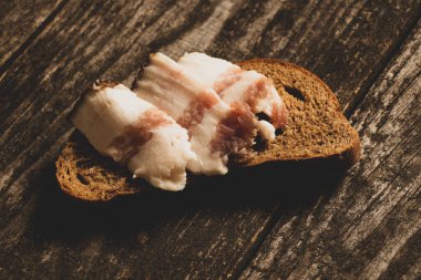 Bir parça siyah ekmek ve dilimlenmiş pastırma tahtadan bir masanın üzerinde, pastırmalı ekmek