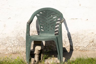 Plastik, eski, kırık bir sandalye, yaz kulübelerinde beyaz bir evin arka planında duruyor. Eski bir sandalye kırık.