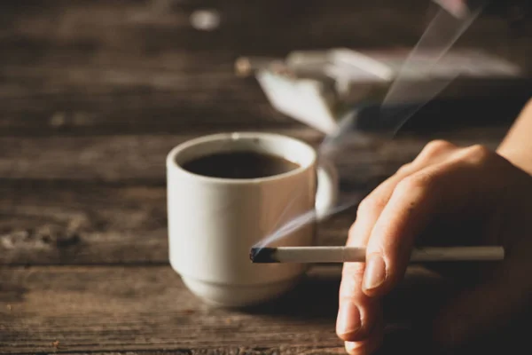 在桌上的一个姑娘手里拿着一支香烟 旁边是一杯咖啡 香烟和咖啡 坏习惯 — 图库照片