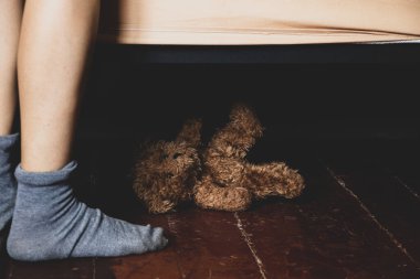 Evin ahşap zemininde yatağın yanında ayaklar ve yatağın altında kahverengi bir oyuncak ayı uzanıyor, ev ve konfor, yerde ayaklar, çocuk odası