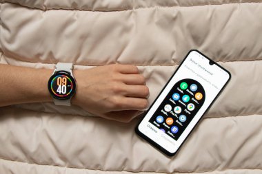 Ukrayna Dnipro 30.11.2021 - Akıllı saat Samsung Galaxy 4.40 mm ve Samsung uygulamalı cep telefonu kızın elinde, teknoloji