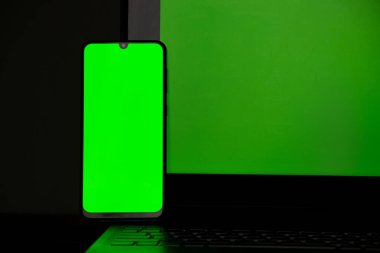 Masadaki siyah dizüstünde yeşil ekranlı bir telefon, yeşil ekranlı bir telefon şeması var.