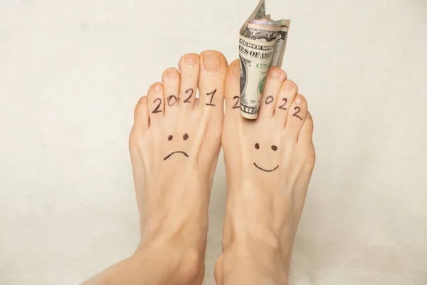 白い背景とドルの指に女の子の足に描かれた2021と2022悲しいと喜びの感情 新年の成功2022 喜びと悲しみ 金融と成功 — ストック写真