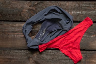 Kadınların eski mavi ve kırmızı külotları ahşap masaya uzanıyor, kadın iç çamaşırları giyiliyor.