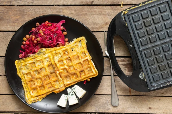 fry scrambled eggs with cheese and spices in a waffle iron on a wooden table in the kitchen, boil scrambled eggs in a waffle iron, breakfast