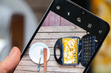 Çırpılmış yumurta, peynirli ve baharatlı waffle ızgarası ahşap arka planda, çırpılmış yumurtaları telefon ekranında kaynatın.